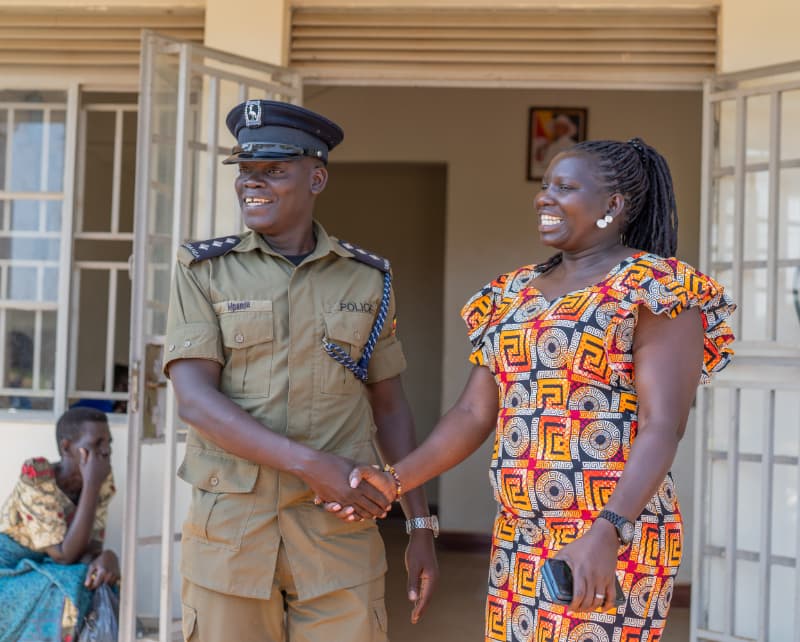 African police officer in uniform shaking hands with woman in colorful patterned dress during community outreach visit.