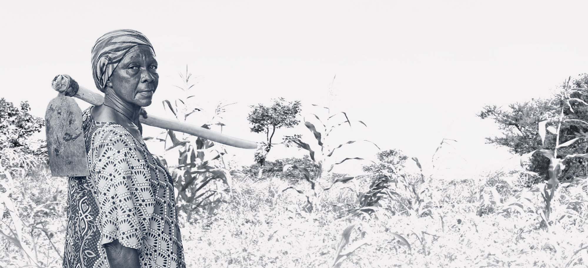 Widow in front of her land with a farming tool