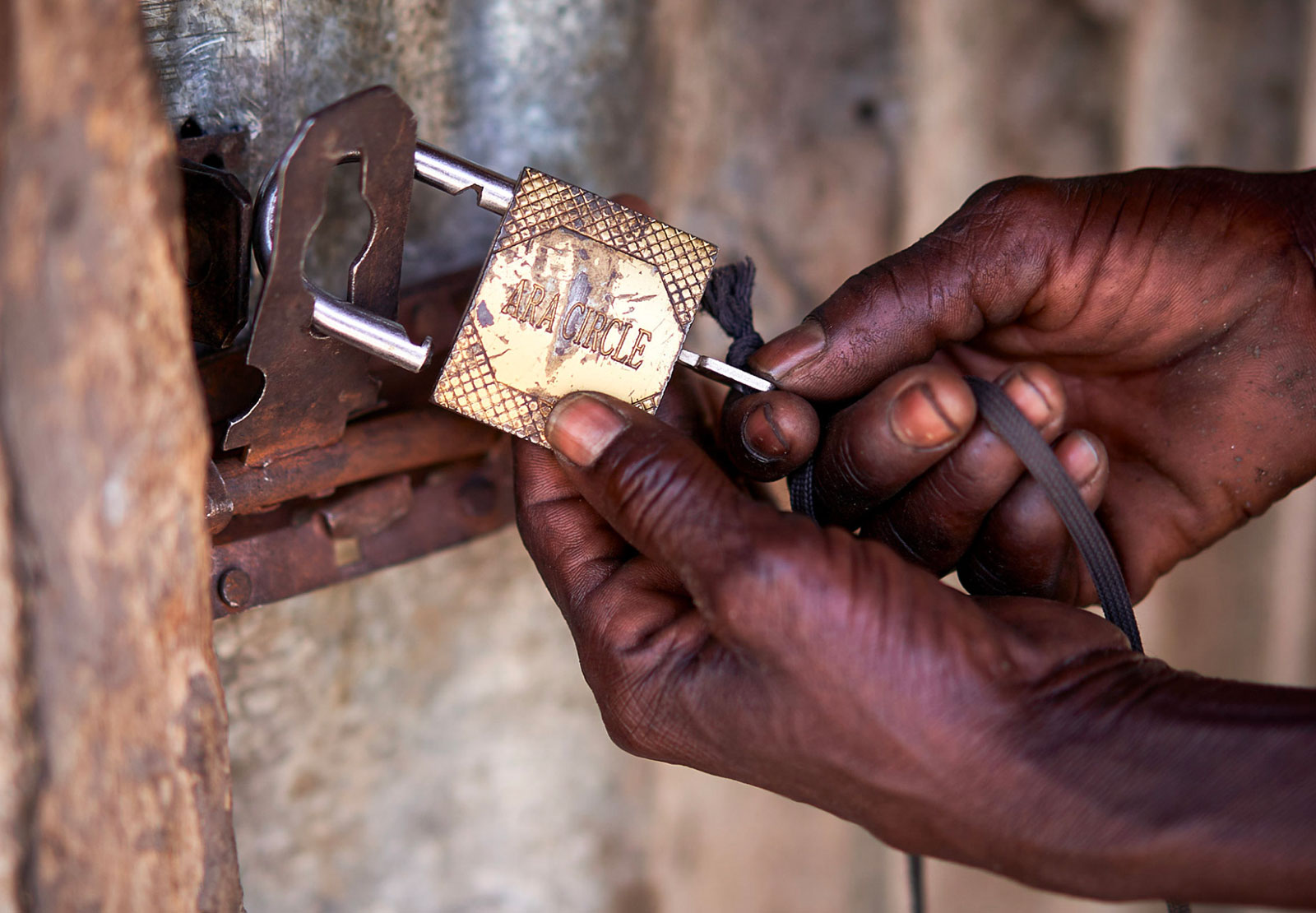 Hands unlocking a padlocked door with a key