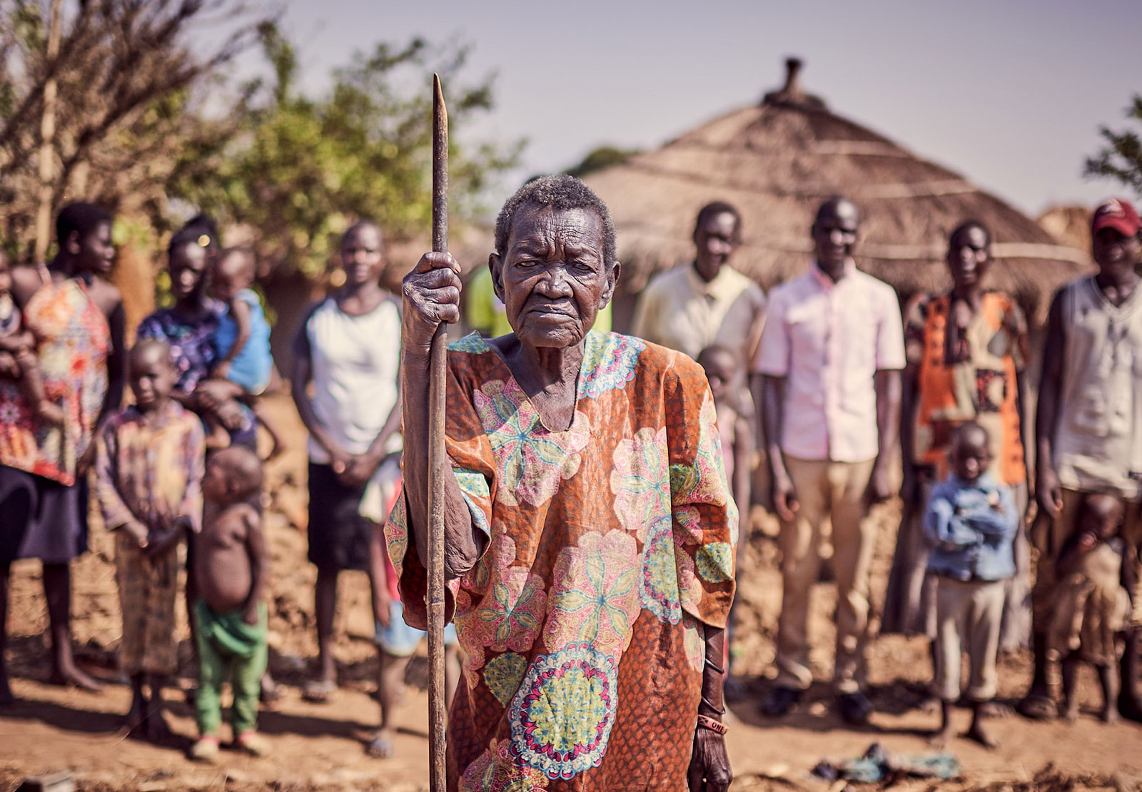 Woman with staff in foreground, group of community members in the background